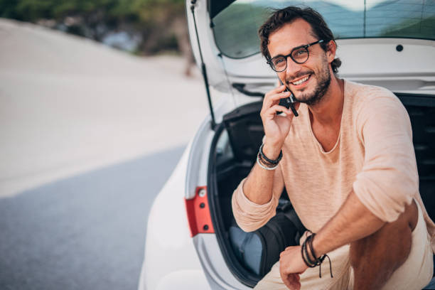 istock Man sitting on car trunk and talking on phone 1191403515