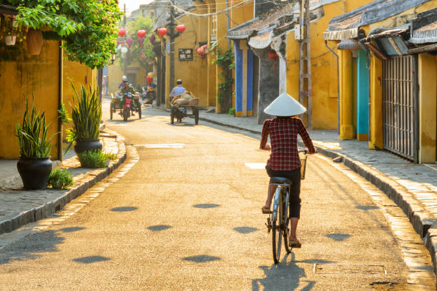 wietnamska kobieta w tradycyjnym kapeluszu na rowerze wzdłuż hoi an - vietnam hoi an traditional culture travel zdjęcia i obrazy z banku zdjęć