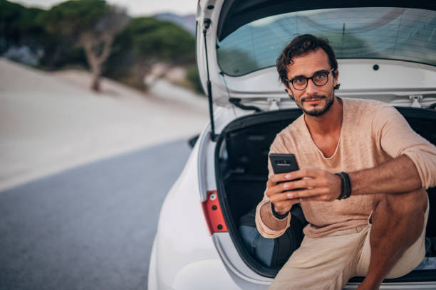 istock Young man sitting on car trunk 1191404977