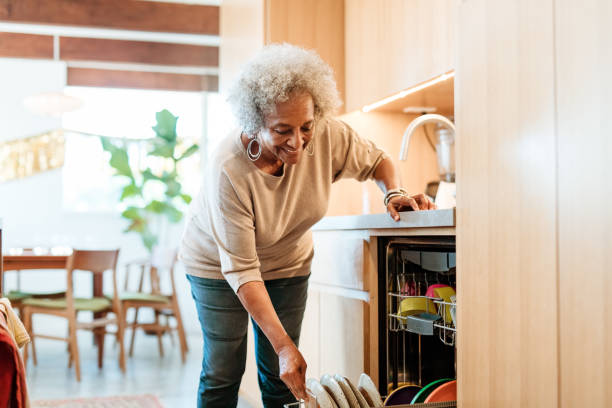 食器洗い機で皿を持っている笑顔の先輩女性 - cleaning domestic kitchen counter top housework ストックフォトと画像