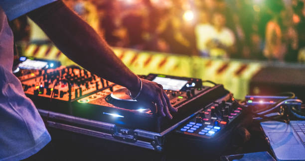 dj mezclando al aire libre en el festival de fiesta de año nuevo con la multitud de personas en el fondo - vista nocturna de discoteca al aire libre - enfoque suave en pulsera, mano - diversión, juventud, entretenimiento y concepto de festival - batidora eléctrica fotografías e imágenes de stock