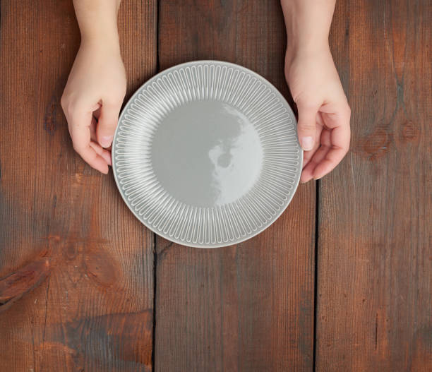 istock hands hold empty gray round ceramic plate, wooden background 1191412978