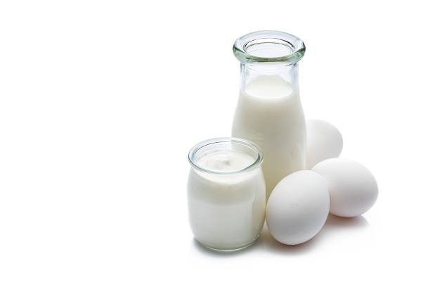 Dairy products: high angle view of a milk bottle, yogurt and white eggs isolated on white background. The composition is at the right of an horizontal frame leaving useful copy space for text and/or logo at the left. Predominant color is white. High resolution 42Mp studio digital capture taken with Sony A7rii and Sony FE 90mm f2.8 macro G OSS lens