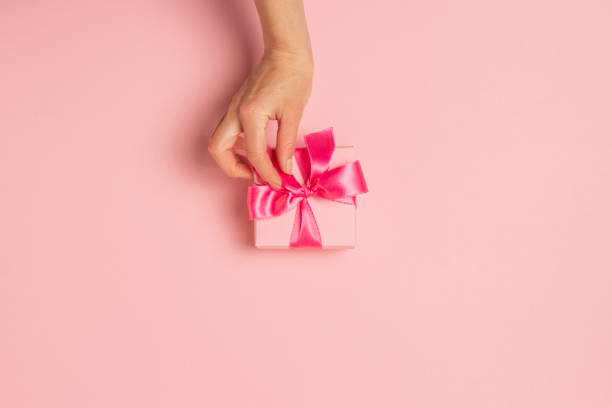 istock Female hands hold, take, receive a gift on a pink background. Wedding concept, Valentine's Day, a gift for a loved one. Flat lay, top view 1191414678