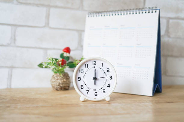 istock white analog clock with blurred calendar on wooden table 1191415495