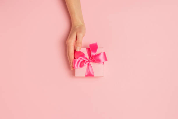 istock Female hands hold, take, receive a gift on a pink background. Wedding concept, Valentine's Day, a gift for a loved one. Flat lay, top view 1191415564