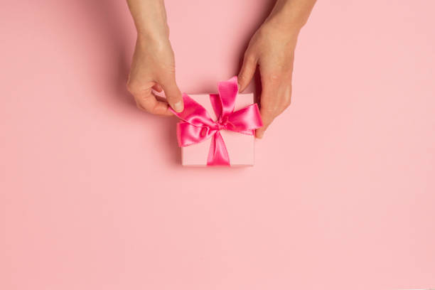 istock Female hands hold, take, receive a gift on a pink background. Wedding concept, Valentine's Day, a gift for a loved one. Flat lay, top view 1191415799