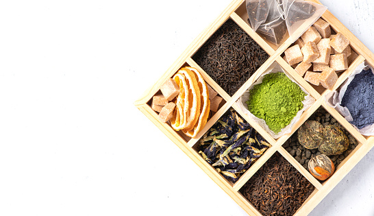 Different types of tea in a wooden box on a light background, top view. Black tea, puer, blue and green matcha tea, green tea and cane sugar.