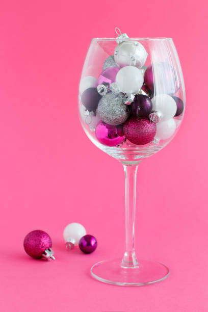istock Christmas baubles in a wine glass on a pink background 1191420013