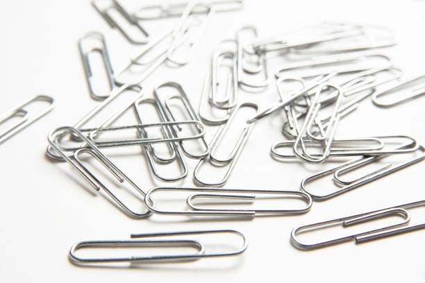 A bunch of silver-color metal paper clips scattered on a plain white background.