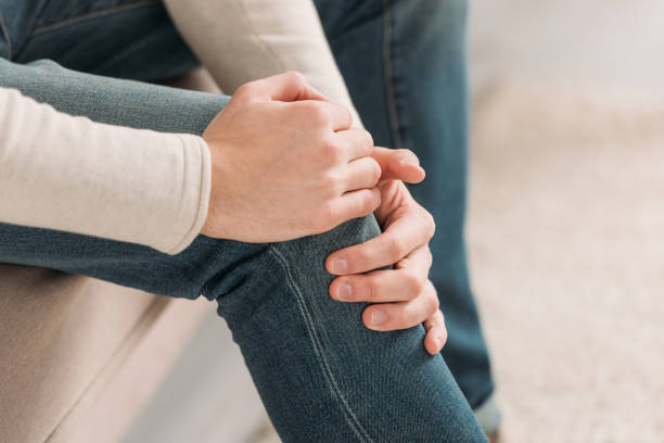 istock cropped view of man sitting on sofa and touching knee while suffering from pain 1191423703