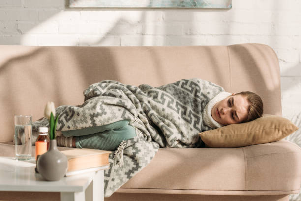 istock sick woman lying on sofa under blanket near table with medicines 1191423756