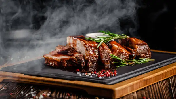 Photo of American food concept. Grilled pork ribs with grilled sauce, with smoke, spices and rosemary. Background image. copy space