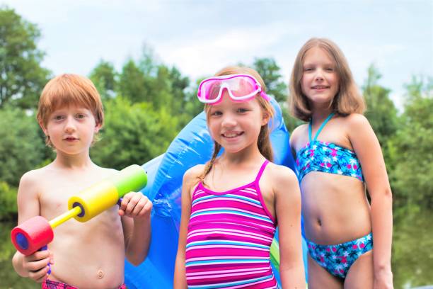 retrato de amigos sonrientes en traje de baño de pie con balsa de la piscina y pistola de chorros a orillas del lago - child inflatable raft lake family fotografías e imágenes de stock