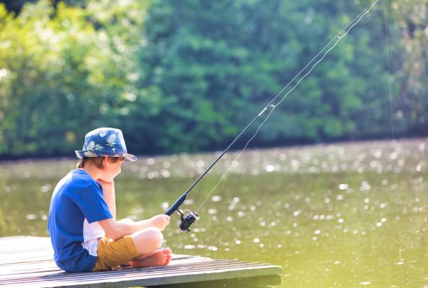 istock Young boy fishing in lake while sitting on pier 1191428337