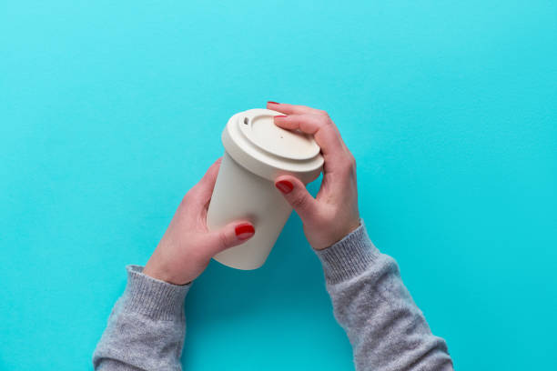 istock Hands holding reusable coffee cup made from eco friendly bamboo with silicone lid. Eco friendly zero waste tea mug on blue mint paper without plastic. Travel solution for sustainable lifestyle. 1191429544