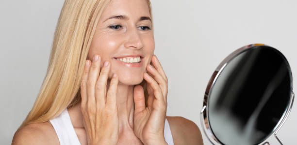 istock Happy middle-aged lady looking at mirror and applying cream 1191430922