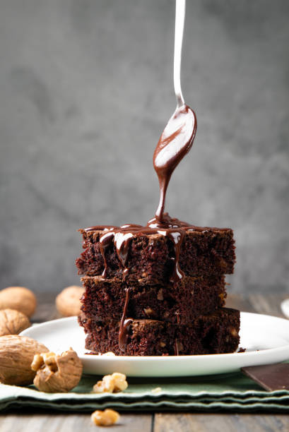 gießen geschmolzener schokolade auf brownies mit einem löffel - brownie baked bakery brown stock-fotos und bilder