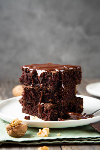 Stack of brownies with melted chocolate Chocolate spongy brownie cakes with walnuts and melted chocolate topping on a stack walnut cookies stock pictures, royalty-free photos & images