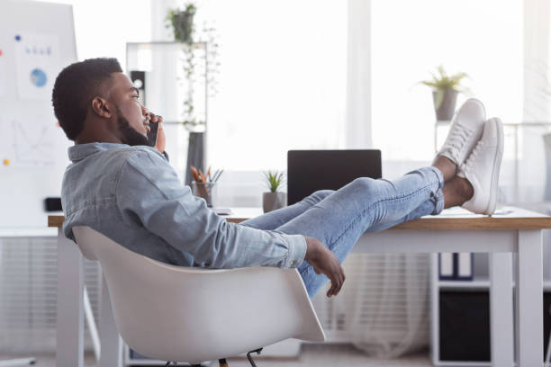 istock Lazy afro worker talking on cellphone with his feet on desk 1191434450