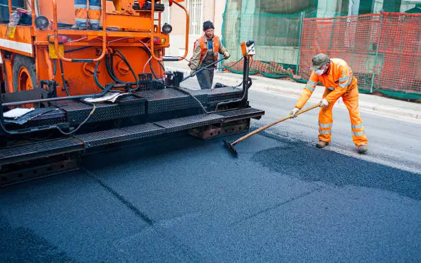 Worker regulate tracked paver laying asphalt heated to temperatures above 160 grades Celsius pavement on a runway