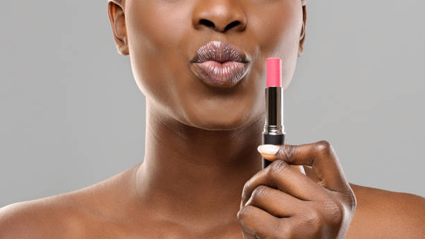 czarna kobieta trzymająca różową szminkę i pouting usta na szarym tle - make up fashion beauty sullen zdjęcia i obrazy z banku zdjęć