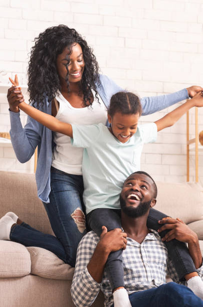 joyful afro parents and their little daughter having fun at home - simple living imagens e fotografias de stock