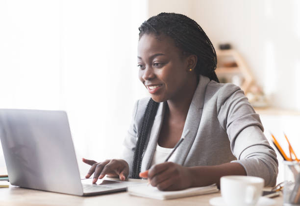 istock Smiling Black Businesswoman Working On Laptop And Taking Notes In Office. 1191436549