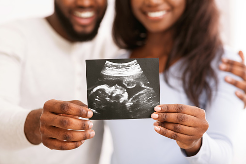 First portrait of our baby. Happy african couple holding sonogram picture, cropped