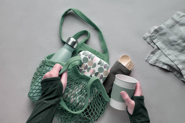 Zero waste packed lunch kit in mesh bag. Net bag with insulated metal water bottle, bamboo cutlery, bamboo lunch box and reusable cup. Sustainable lifestyle, flat lay, top view on recycled craft paper kit de almuerzo para llevar de cero residuos, lonchera para llevar en bolsa de algodón, organizador de cubiertos de bambú, lonchera de bambú y taza reutilizable. estilo de vida sostenible, plano geométrico, vista superior sobre papel artesanal.