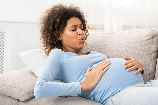 Expectant woman having contractions and doing breathing exercises, lying on sofa at home