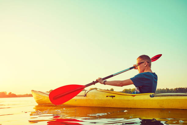 le persone kayak durante il tramonto sullo sfondo. divertiti nel tuo tempo libero. - men sitting canoe canoeing foto e immagini stock