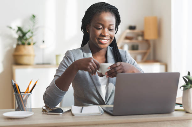 istock Black businesswoman drinking coffee while working on laptop in modern office 1191441697