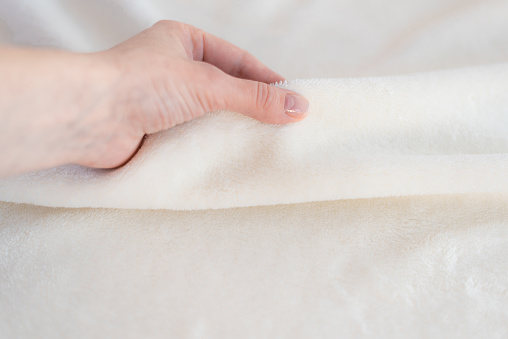 Female hand touches a soft cozy plaid of white fabric with a pile. Textile material, pleasant to the touch