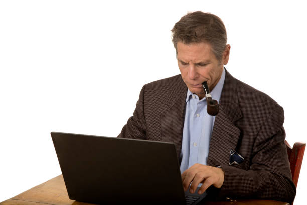 istock Man at table looking down with pipe in mouth on laptop typing 1191450218