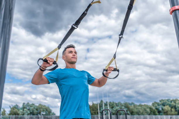 istock Male athlete, pulls himself on hinges, push-ups on elastic bands trx strap, in summer in city. Fitness motivation youth lifestyle. Free space for copy text. Sportswear T-shirt. 1191451539