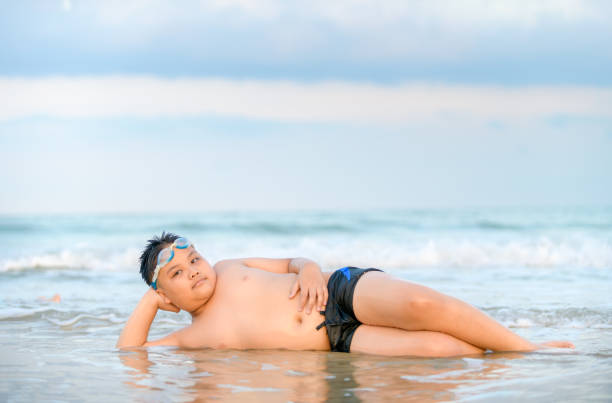 cute asian obese boy playing wave on beach, travel and relax concept