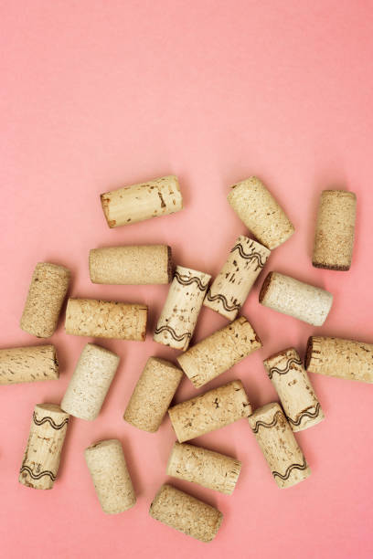 Used wine corks on pink paper background with copy space. Top view with wooden corks from bottle of wine. Flat lay.