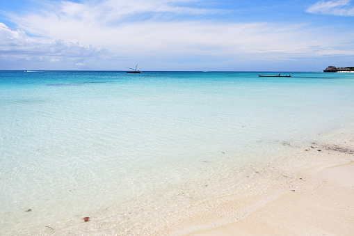 Azure ocean waters transition from turquoise to deeper shades of blue, gently rippling under the bright sky. The view captures the vastness and tranquility of the seascape, devoid of any visible land. The horizon stretches into the distance where the sky meets the sea. Shot taken in Nusa Dua, Bali.