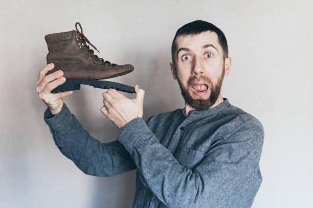 istock Man holding an old leather boot with torn sole, surprise and shock on his face 1191456103