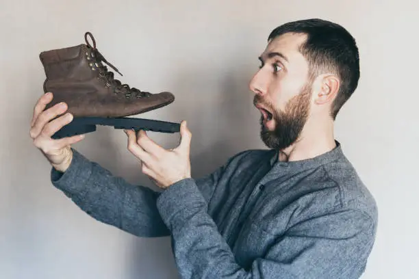 Photo of Man looking at an old leather boot with torn sole, surprise and shock on his face