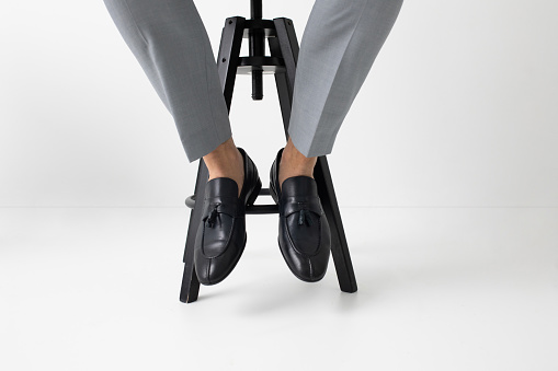 Legs of unrecognisable elegant man sitting on chair and wearing loafers.