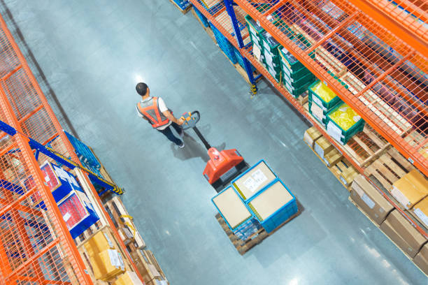 High angle view of Male warehouse worker. High angle view of Male warehouse worker pulling a pallet truck at distribution warehouse. hardware store photos stock pictures, royalty-free photos & images