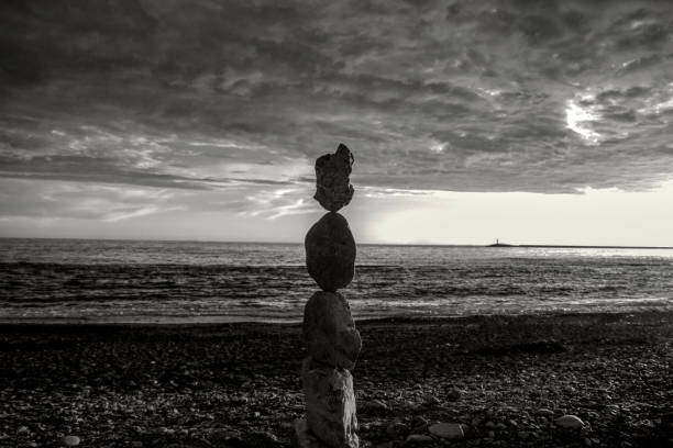 black and white photo pyramid of large stones on the beach at sunset