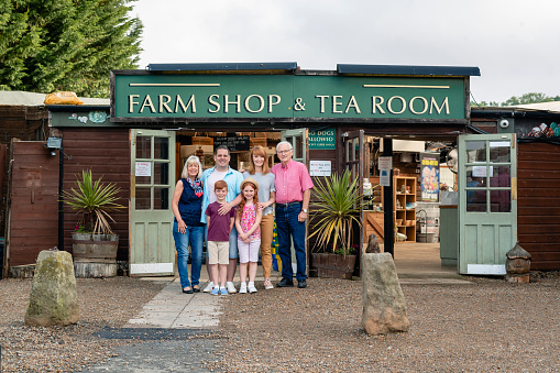 A three-generation family posing for a picture together while smiling outside a farm shop.