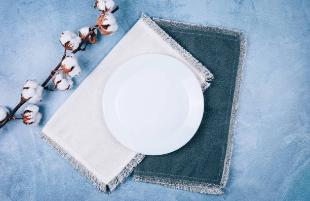 istock Empty circle plate on linen napkins decorated with cotton flowers on blue grey background. 1191460553