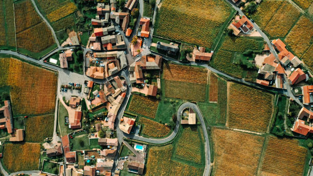 Aerial shot of a French village with orange roofs, winding roads and surrounded by vineyards - stock photo Drone photo of a small wine producing village near Macon in Burgundy, France. village stock pictures, royalty-free photos & images