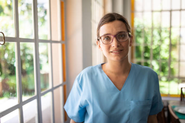 Smiling Argentinian female nurse standing near window Smiling Argentinian female nurse with eyeglasses, in blue uniform  standing near window, looking happily in camera argentinian ethnicity photos stock pictures, royalty-free photos & images