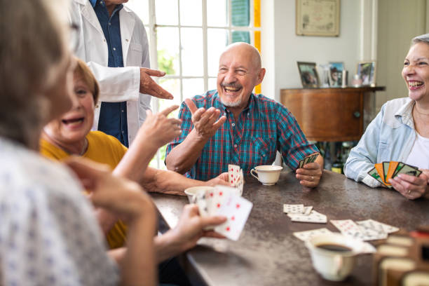 godersi il loro gioco di carte in casa di cura - nursing home senior adult group of people home caregiver foto e immagini stock