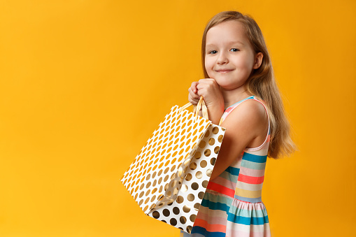 Little girl holds a paper bag. The child close up in a summer dress on a yellow background.